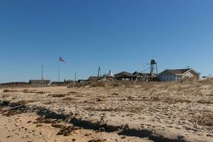 I love the look of this beautiful beach scene.. The sea debris lay scattered around with the pretty sand all around. The brown sand dunes in the background and small village. photo