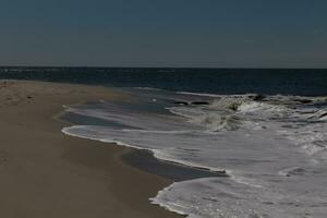 I loved the look of this beach scene as the waves crashed in. The pretty look of the whitecapped surf rushing in to the shore. The sand showing a different tone to where the water once was. photo