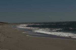 This beautiful beach image was taken at Cape May New Jersey. It shows the waves rippling into the shore and the pretty brown sand. The blue sky with the little bit of cloud coverage adds to this. photo