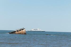 Image taken at Sunset beach in Cape May New Jersey. The sunken ship seen off the coast protruding from the water. The brown rusty hull looking weathered. Cape May Lewes ferry seen passing by. photo