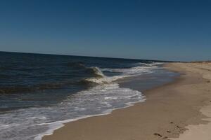 This beautiful beach image was taken at Cape May New Jersey. It shows the waves rippling into the shore and the pretty brown sand. The blue sky with the little bit of cloud coverage adds to this. photo