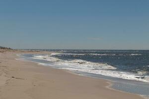 This beautiful beach image was taken at Cape May New Jersey. It shows the waves rippling into the shore and the pretty brown sand. The blue sky with the little bit of cloud coverage adds to this. photo