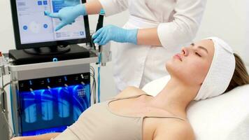 Cosmetology clinic. Professional female cosmetologist doing hydrafacial procedure while being a work. Attractive nice woman lying on the medical bed while having beauty procedures video