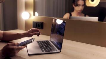 Woman using mobile phone while working at home with laptop. Person sit at workplace desk holds cellphone staring at laptop, synchronize data between computer and gadget video