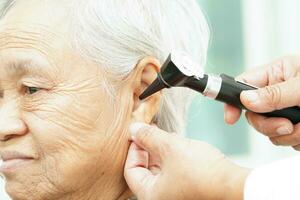 Otolaryngologist or ENT physician doctor examining senior patient ear with otoscope, hearing loss problem. photo