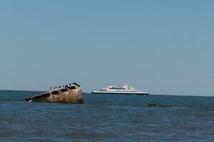 Image taken at Sunset beach in Cape May New Jersey. The sunken ship seen off the coast protruding from the water. The brown rusty hull looking weathered. Cape May Lewes ferry seen passing by. photo