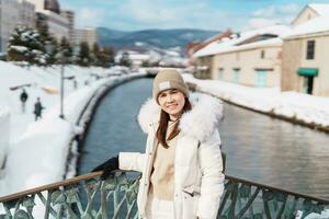 Woman tourist Visiting in Otaru, happy Traveler in Sweater sightseeing Otaru canal with Snow in winter season. landmark and popular for attractions in Hokkaido, Japan. Travel and Vacation concept photo