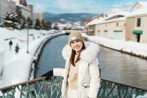 Woman tourist Visiting in Otaru, happy Traveler in Sweater sightseeing Otaru canal with Snow in winter season. landmark and popular for attractions in Hokkaido, Japan. Travel and Vacation concept photo