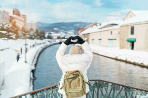 Woman tourist Visiting in Otaru, happy Traveler in Sweater sightseeing Otaru canal with Snow in winter season. landmark and popular for attractions in Hokkaido, Japan. Travel and Vacation concept photo