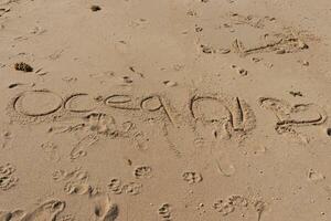 Beautiful brown sand with writing etched in. The word ocean can be seen written ion the beach. Footprints can be seen all around. photo