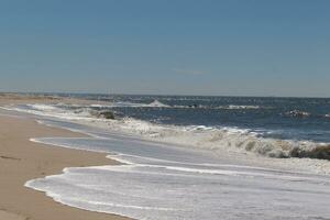 I loved the look of this beach scene as the waves crashed in. The pretty look of the whitecapped surf rushing in to the shore. The sand showing a different tone to where the water once was. photo