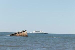 Image taken at Sunset beach in Cape May New Jersey. The sunken ship seen off the coast protruding from the water. The brown rusty hull looking weathered. Cape May Lewes ferry seen passing by. photo