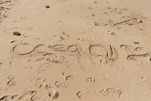 Beautiful brown sand with writing etched in. The word ocean can be seen written ion the beach. Footprints can be seen all around. photo