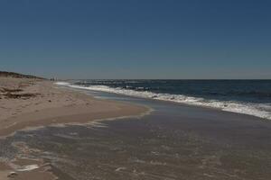 This beautiful beach image was taken at Cape May New Jersey. It shows the waves rippling into the shore and the pretty brown sand. The blue sky with the little bit of cloud coverage adds to this. photo