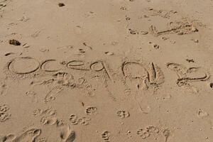 Beautiful brown sand with writing etched in. The word ocean can be seen written ion the beach. Footprints can be seen all around. photo