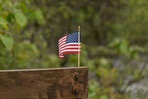 This is an image of a small American flag pinned to a wooden beam. This patriotic display looks quire colorful with the red, white, and blue. The symbol of American is gently flowing in the breeze. photo