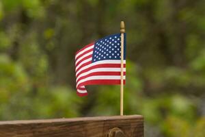This is an image of a small American flag pinned to a wooden beam. This patriotic display looks quire colorful with the red, white, and blue. The symbol of American is gently flowing in the breeze. photo