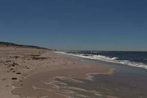 This beautiful beach image was taken at Cape May New Jersey. It shows the waves rippling into the shore and the pretty brown sand. The blue sky with the little bit of cloud coverage adds to this. photo