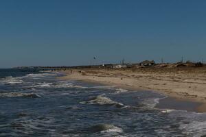 I loved the look of this beautiful beach scene. with pretty sand dunes. The water pummeling the shore with looks of rough seas. Whitecaps rippling through with pretty blue skies. photo