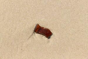 Pretty sea glass sitting on the beach. The red shard of a bottle lay sitting in the sand, washed up from the sea. The edges no longer sharp from the turbulent waters. photo