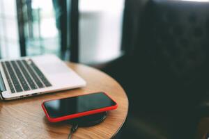 Charging mobile phone battery with wireless device in the table. Smartphone charging on a charging pad. Mobile phone near wireless charger. photo