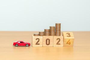 2023 flipping to 2024 year block with car model and Coins Money stack for deposit and Automobile Tax. Money Saving, Car Insurance, Financial, vehicle Repair and Maintenance and New Year concept photo