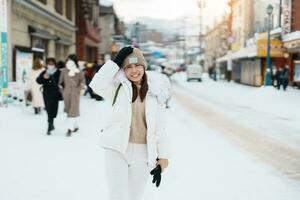 mujer turista visitando en otaru, contento viajero en suéter Turismo otaru ciudad con nieve en invierno estación. punto de referencia y popular para atracciones en Hokkaidō, Japón. viaje y vacaciones concepto foto