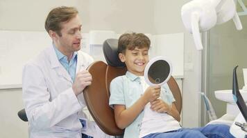 Lovely boy checking out his healthy teeth in the mirror after dental examination video