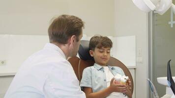 Mature dentist smiling to the camera while working with adorable little boy video