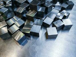 Montón de pequeños cubos de acero brillante mecanizado sobre superficie metálica foto