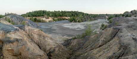 eroded soil quarry ravine with forest on its edge at summer evening panoramic photo