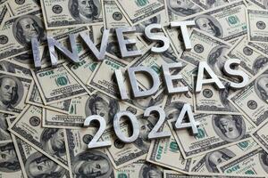 words invest ideas 2024 laid with thick metal letters on the US dollar bills background - with selective focus and diagonal composition. photo