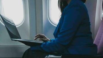 Successful beautiful young asian business woman sits in airplane cabinplane and works on digital tablet with stylus. Flying at first class. video