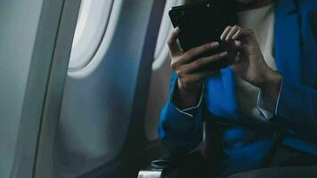 in viaggio e tecnologia. volante a primo classe. bella giovane imprenditori donna utilizzando smartphone mentre seduta nel aereo. video
