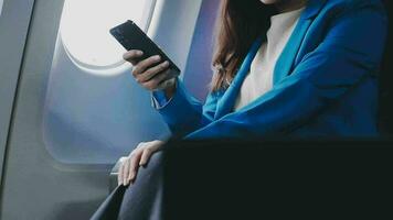 de viaje y tecnología. volador a primero clase. bonito joven businees mujer utilizando teléfono inteligente mientras sentado en avión. video