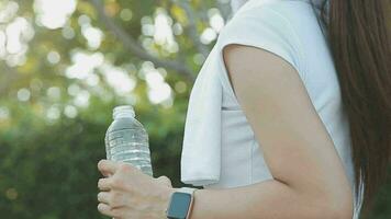 jovem mulher atleta leva uma quebrar, bebendo água, Fora em uma corre em uma quente dia. video