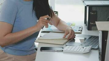 affascinante giovane asiatico donna d'affari seduta su il computer portatile computer nel il ufficio, fabbricazione rapporto calcolatore equilibrio interno reddito servizio controllo documento. video