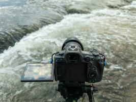 modern black digital mirrorless camera with flip-screen on tripod capturing streaming water, closeup photo