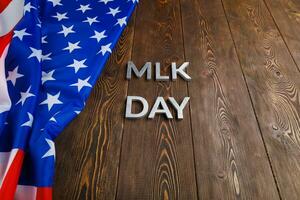 la palabra mlk day colocada con letras de metal plateado sobre una superficie de madera con una bandera de estados unidos arrugada en el lado izquierdo foto