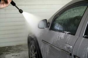 Indoor car washing. Process of removing soap foam from side of vehicle with pressure washer - close-up with selective focus. photo