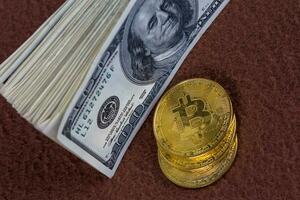 bunch of us dollar banknotes and three bitcoin shiners on brown fleece background close-up with selective focus photo