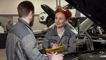 Lovely female mechanic taking notes, talking to a colleague at the garage video