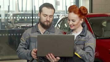 Bearded car mechanic using laptop at the garage, working with female colleague video