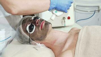 Man getting facial carbon peeling at beauty clinic by professional cosmetologist video