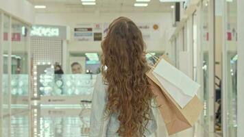 traseiro Visão tiro do uma encaracolado cabelos pequeno menina olhando às roupas lojas às compras Shopping video