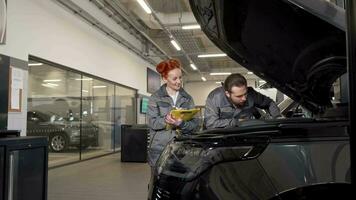 Two professional car mechanics examining engine of a car, making notes video