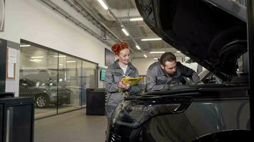 twee professioneel auto mechanica onderzoeken motor van een auto, maken aantekeningen video