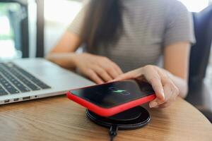 Charging mobile phone battery with wireless device in the table. Smartphone charging on a charging pad. Mobile phone near wireless charger. photo