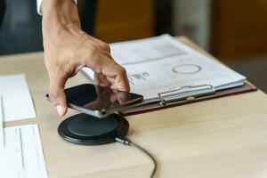 Charging mobile phone battery with wireless charging device in the table. Smartphone charging on a charging pad. Mobile phone near wireless charger Modern lifestyle technology concept photo