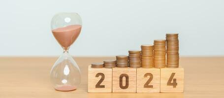 Happy New Year with sandglass and flipping 2023 change to 2024 block. Resolution, Goals, Plan, Action, Money Saving, Retirement fund, Pension, Investment and Financial concept photo